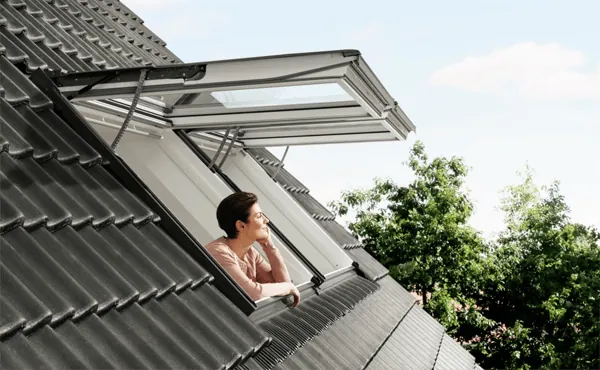 vrouw die in Elektrische VELUX uitzettuimelvenster staat en naar buiten kijkt